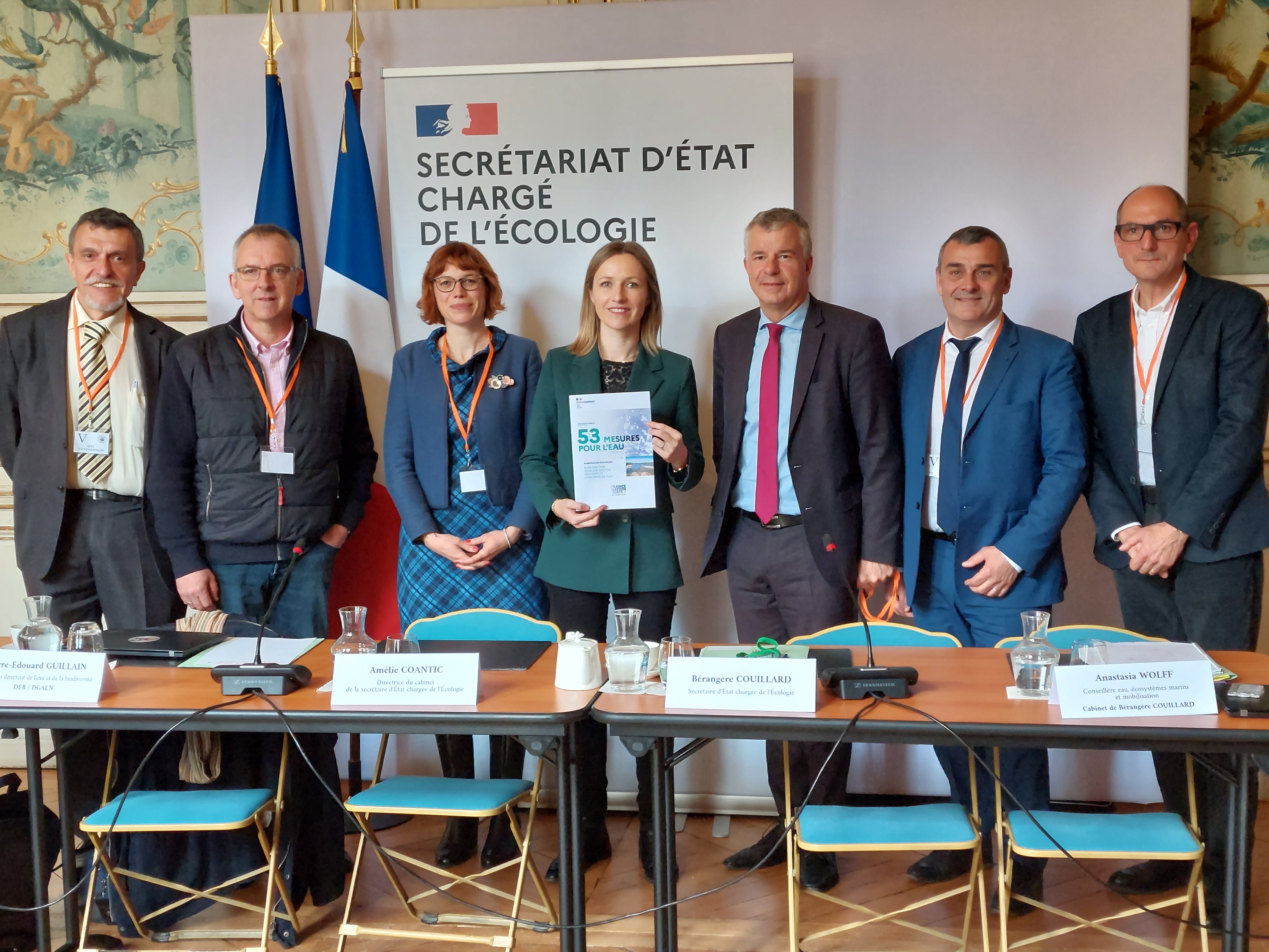 2 femmes et 5 hommes derrière un bureau avec le plan eau. 